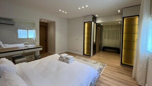 Quarto de hotel moderno com uma cama grande, mesa de cabeceira, espelho e closet espaçoso.