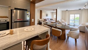 Cozinha moderna com ilha central, área de refeições com cadeiras e sala de estar com sofás.