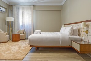 A hotel room with a large bed, a bedside table, a lamp, a chair, and a floor lamp. - Luxury APT - 3BR - South Teseen I (New Cairo)