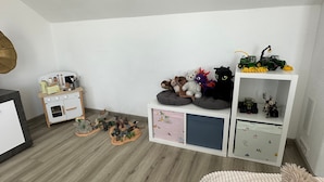 Une salle de jeux pour enfants avec un mur blanc, une cuisine miniature et une étagère remplie de jouets et de figurines.