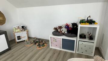Ein Kinderzimmer mit weißer Wand, einer Spielküche und einem Regal voller Spielzeug und Figuren.