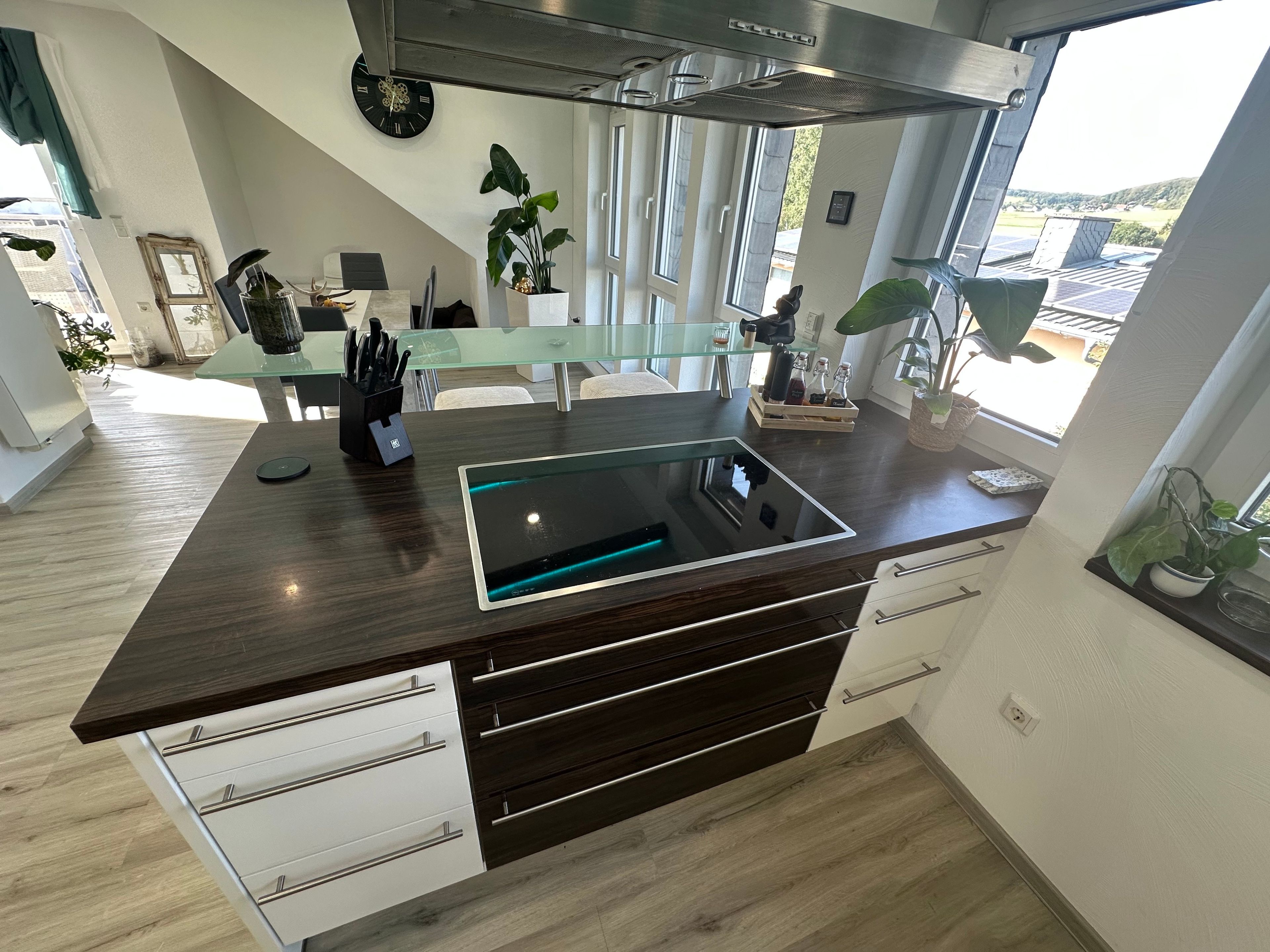 A modern kitchen with a dark wood countertop, a built-in induction cooktop, and a view of the countryside through large windows.