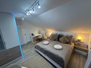 Ein modernes Schlafzimmer mit Bett, Nachttischen, Schreibtisch und Kleiderschrank.