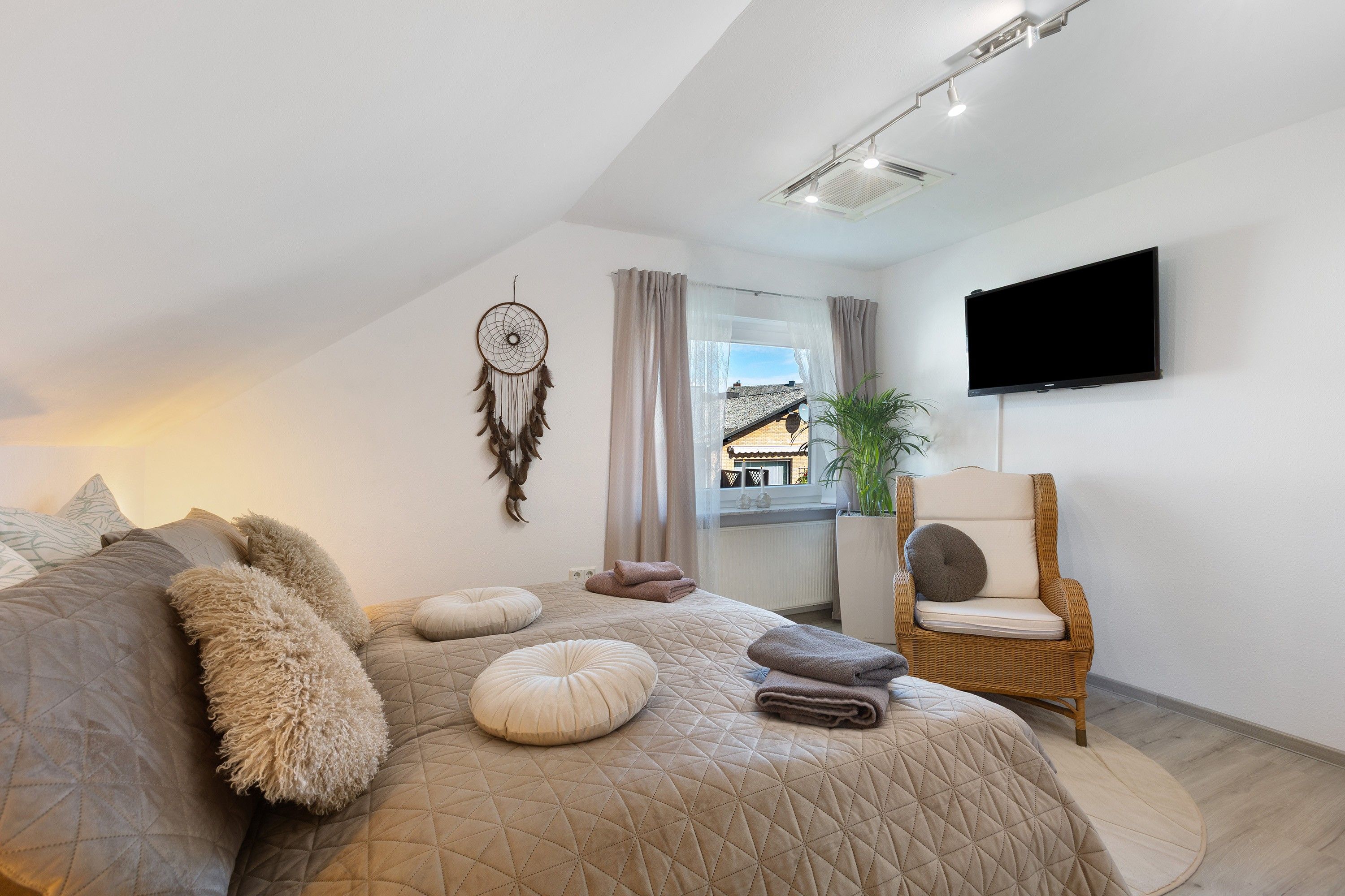 Een slaapkamer met een groot bed, een dromenvanger, een stoel en een televisie.