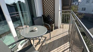 Un balcone con una porta vetrata, un tavolo rotondo, due sedie e una ringhiera in metallo.