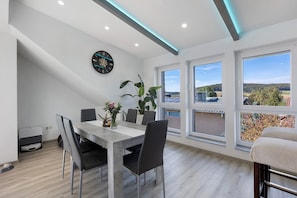 A modern dining area with a table, chairs, a clock, and large windows offering a view.