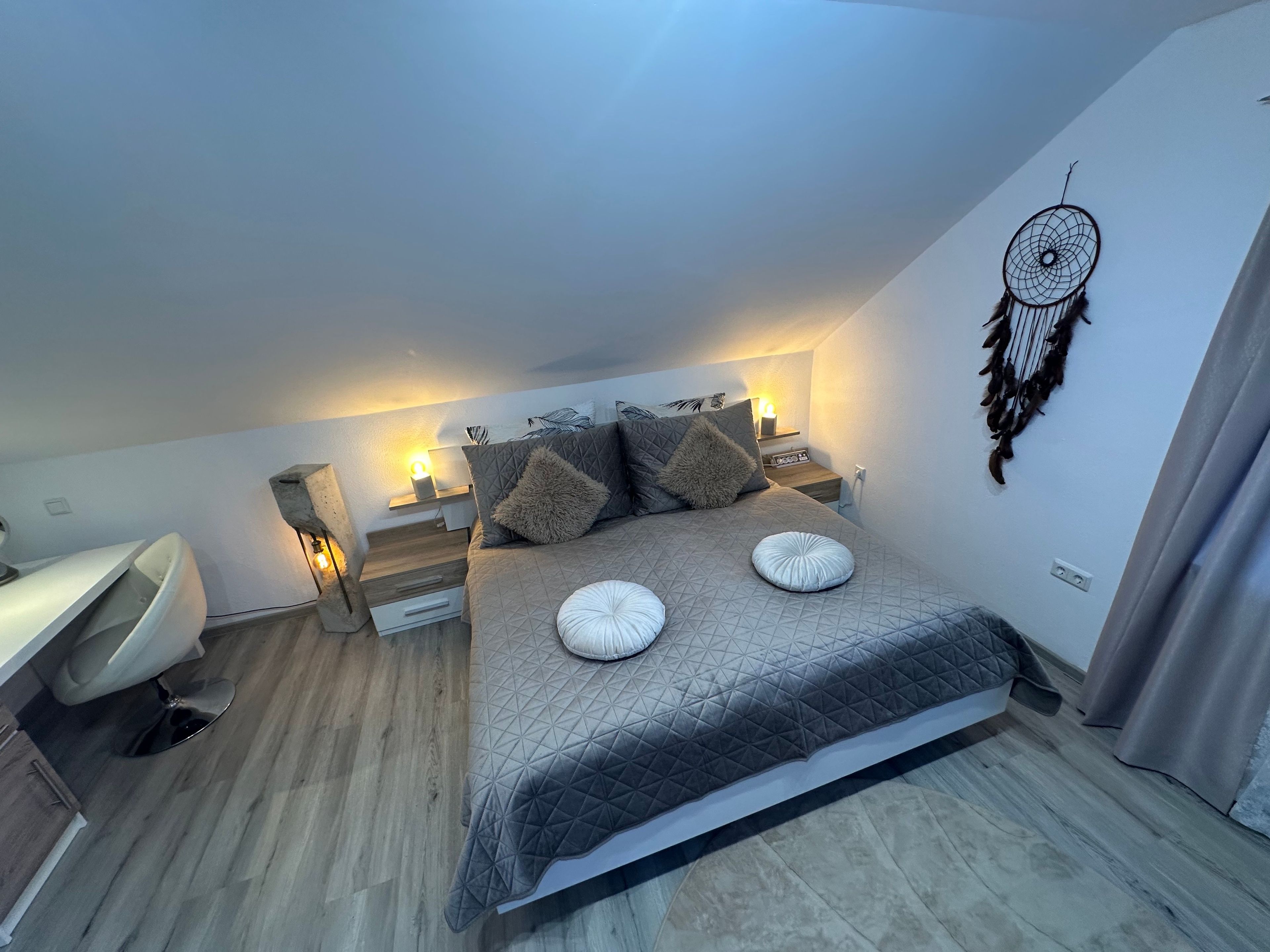 Une chambre à coucher avec un lit, des tables de chevet, un attrape-rêves et un bureau.