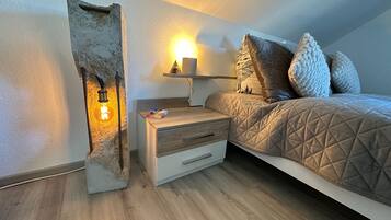 Quarto com cama, mesa de cabeceira, luminária e prateleira na parede.
