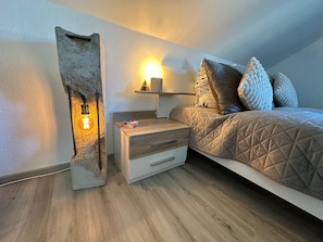 A bedroom with a bed, a nightstand, a lamp, and a wall-mounted shelf.