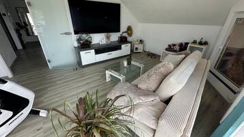 Un salon moderne avec un grand téléviseur à écran plat, un canapé, une table basse et une plante en pot.