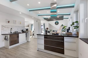 A modern kitchen with a central island, white cabinetry, and a stainless steel range hood.