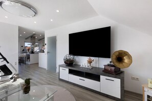 A modern living room with a flat-screen TV mounted on the wall, a gramophone on a console table, and a glass coffee table with a plant.