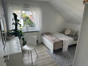 Een slaapkamer met een bed, een stoel, een raam met gordijnen en een radiator.