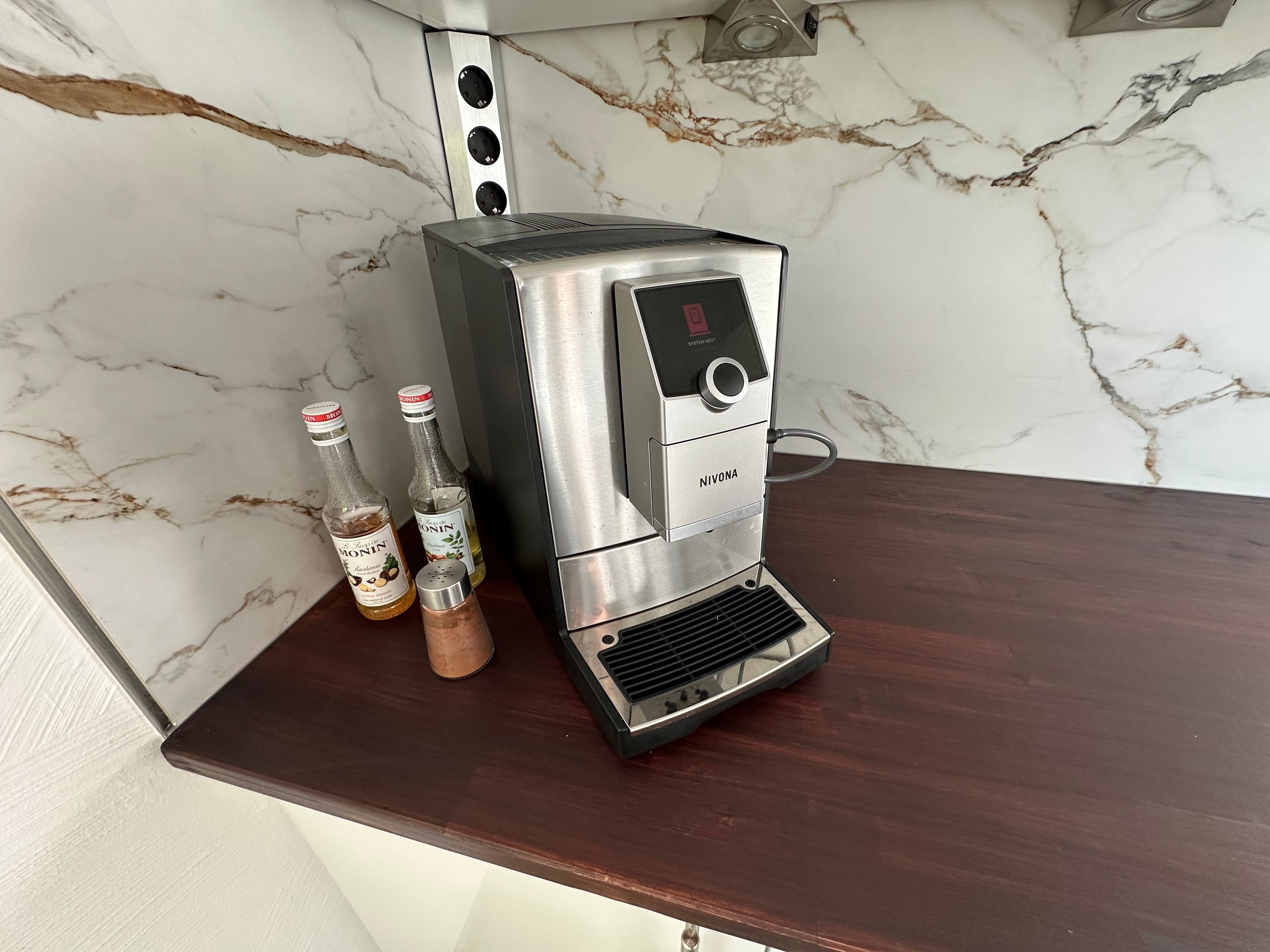 Una màquina de cafè d'acer inoxidable amb pantalla digital, damunt un taulell de fusta.