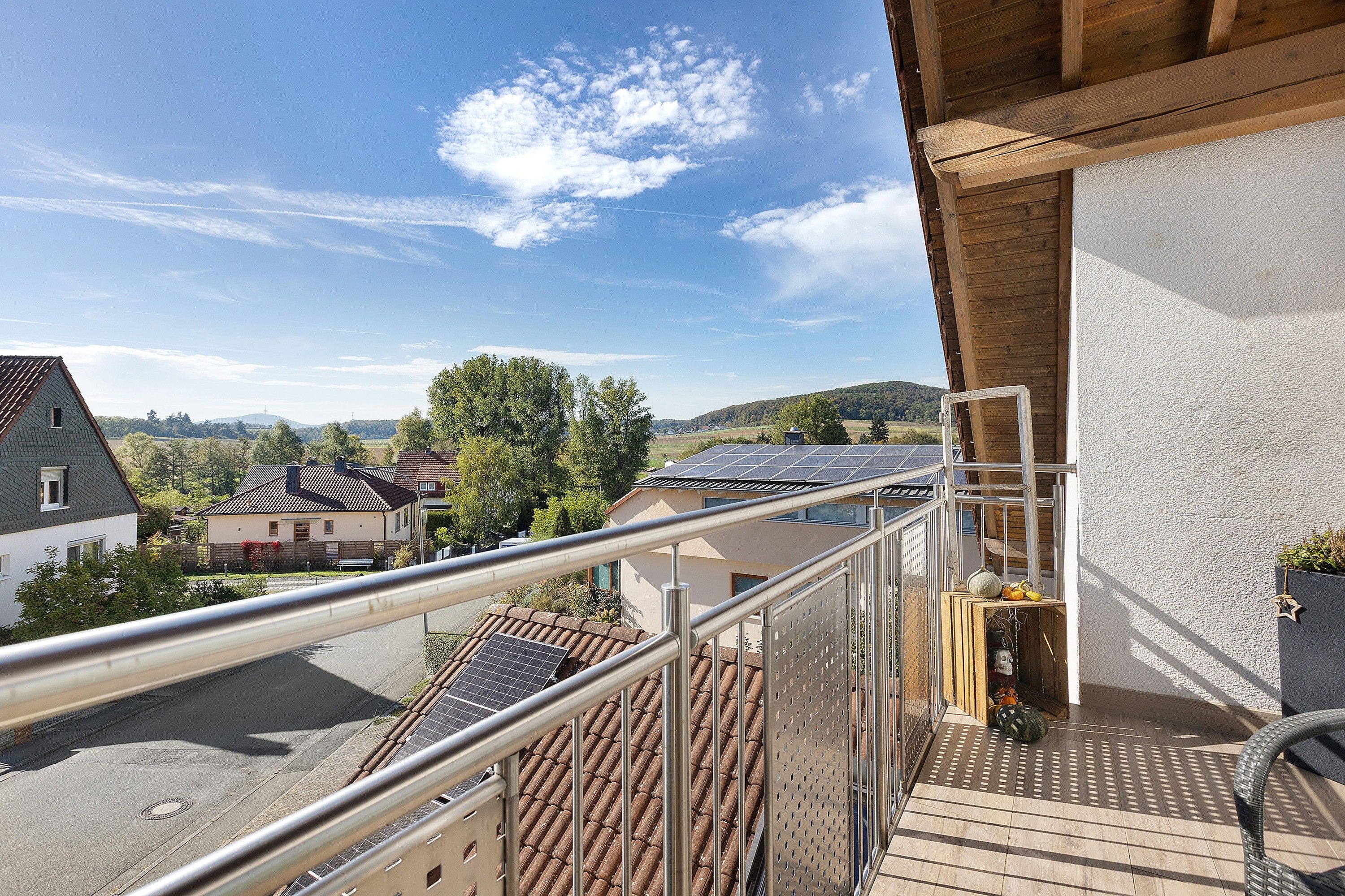Ein Balkon mit Blick auf ein Wohngebiet, einem Metallgeländer und einem Solarpanel auf dem Dach.