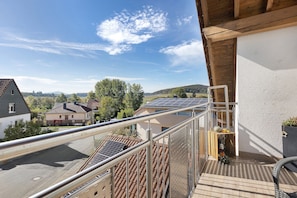 A balcony with a view of a residential area, a metal railing, and a solar panel on the roof.