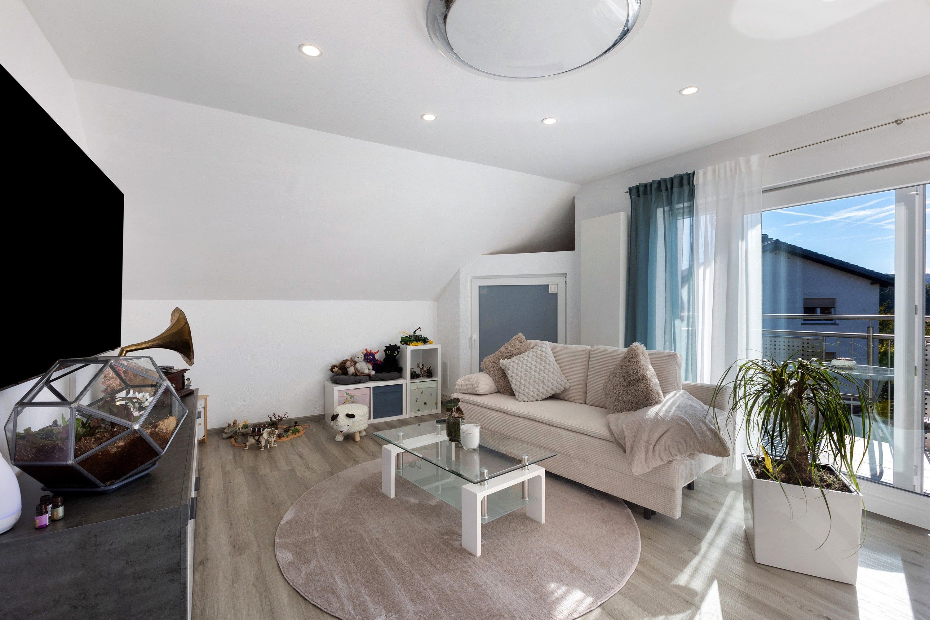Ein modernes Wohnzimmer mit einem Glastisch, einer Couch und einem großen Fenster mit Vorhängen.