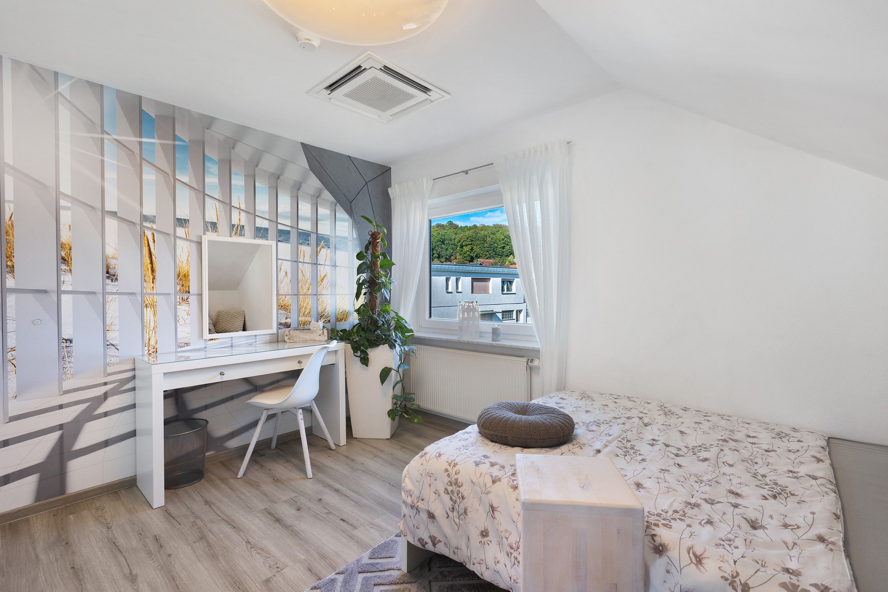 Ein Schlafzimmer mit Bett, Schreibtisch, Stuhl, Heizkörper, einem Fenster mit Vorhängen und Blick nach draußen.