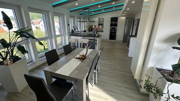 Une cuisine moderne avec des meubles blancs, un îlot central et un coin repas comprenant une longue table et des chaises.