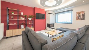 A modern living room with a red accent wall, a fireplace, a flat-screen TV, and a large window. - Vrbo Property (Athina)