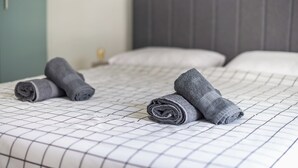 A bed with a white grid-patterned bedspread and two rolled-up towels. - Vrbo Property (Athina)