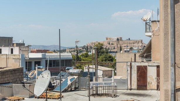 A rooftop with satellite dishes, a building with a door, and a distant view of a historical site. - Vrbo Property (Athina)