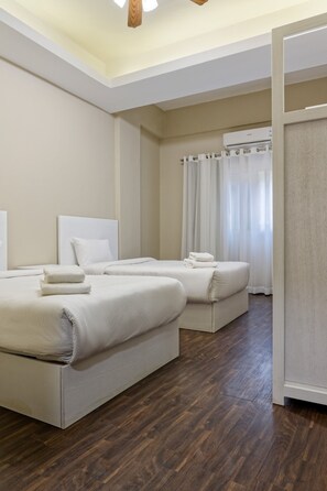 A hotel room with two beds, a ceiling fan, and a view of the street through the window. - Vesta - Luxury APT - 3BR - South Academy III (New Cairo)