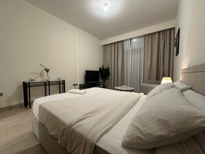 A hotel room with a large bed, a desk with a TV, a small table, and a sofa. - Vesta - Luxury Studio - Riviera I (Dubai)