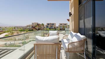 Un balcón con mobiliario de mimbre y barandilla de vidrio con vistas a un área residencial.