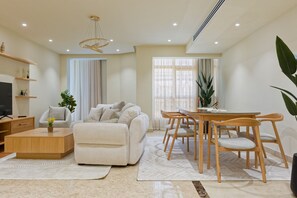 A modern living room with a sofa, coffee table, TV, and dining area with chairs and a table. - Vesta - Luxury APT - 4BR - New Cairo III (New Cairo)