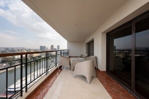 Ein Balkon mit Blick auf einen Fluss und die Stadtlandschaft, ausgestattet mit Korbmöbeln und einer Glastür.