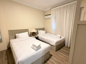 Ein Hotelzimmer mit zwei Betten, einem Nachttisch mit Lampe und einem Fenster mit Vorhängen.