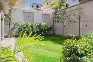 A courtyard with a grassy area, potted plants, and a building facade. - Vesta - Luxury Duplex - 3BR - Zayed City I (6th of October City)