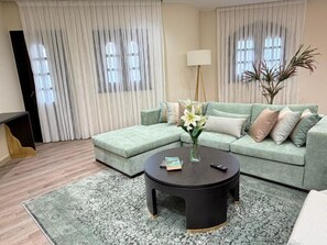 A living room with a green sofa, a round coffee table, and a floor lamp. - Vesta - Luxury APT - 2BR - South Teseen II (New Cairo)