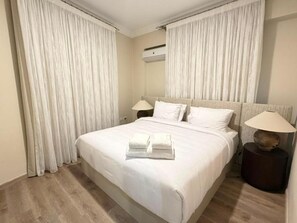 A hotel room with a large bed, two bedside tables, and a window with curtains. - Vesta - Luxury APT - 2BR - South Teseen II (New Cairo)