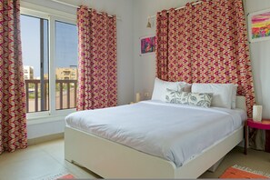 Ein Schlafzimmer mit Bett, Vorhängen, einem Gemälde und Blick auf Gebäude.