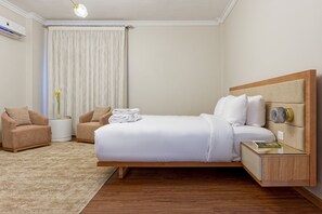 A hotel room with a bed, a chair, a bedside table, and a nightstand. - Vesta - Luxury APT - 3BR - South Teseen III (New Cairo)