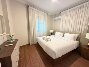 A hotel room with a bed, bedside tables, a dresser, and a window with curtains. - Vesta - Luxury APT - 2BR - South Teseen III (New Cairo)