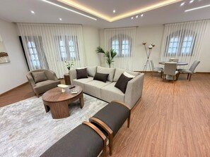 A modern living room with a sectional sofa, a round coffee table, and a dining area with a table and chairs. - Vesta - Luxury APT - 2BR - South Teseen III (New Cairo)