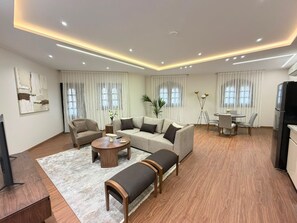 A modern living room with a sofa set, a coffee table, a bench, and a dining area with a table and chairs. - Vesta - Luxury APT - 2BR - South Teseen III (New Cairo)
