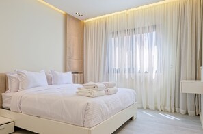 A modern bedroom with a large bed, white bedding, and a neatly made stack of towels. - Vesta - Luxury APT - 3BR - Zayed City II (6th of October City)