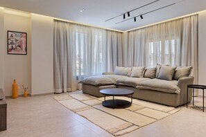 A modern living room with a sectional sofa, a round coffee table, and a large window with sheer curtains. - Luxury Duplex - 3BR - Zayed City II (6th of October City)