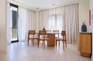 A dining area with a round table and four chairs, a wooden cabinet, and a view through large windows with sheer curtains. - Vesta - Luxury APT - 3BR - Zayed City IV (6th of October City)