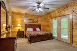A wooden cabin bedroom with a bed, a nightstand, a lamp, a ceiling fan, and a sign indicating a canoe livery. - Spacious 6,000 Sq Ft Log Lodge | Sleeps 27 | Hot Tub, Game Room, Private Wooded (Gatlinburg)