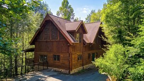 Eine Blockhütte mit Veranda und einem von einem Zaun umgebenen Einfahrtsweg, umgeben von dichtem Wald.