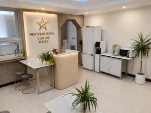 Un espace d’accueil d’hôtel au design moderne, comprenant un comptoir d’accueil, un coin salon et une kitchenette.