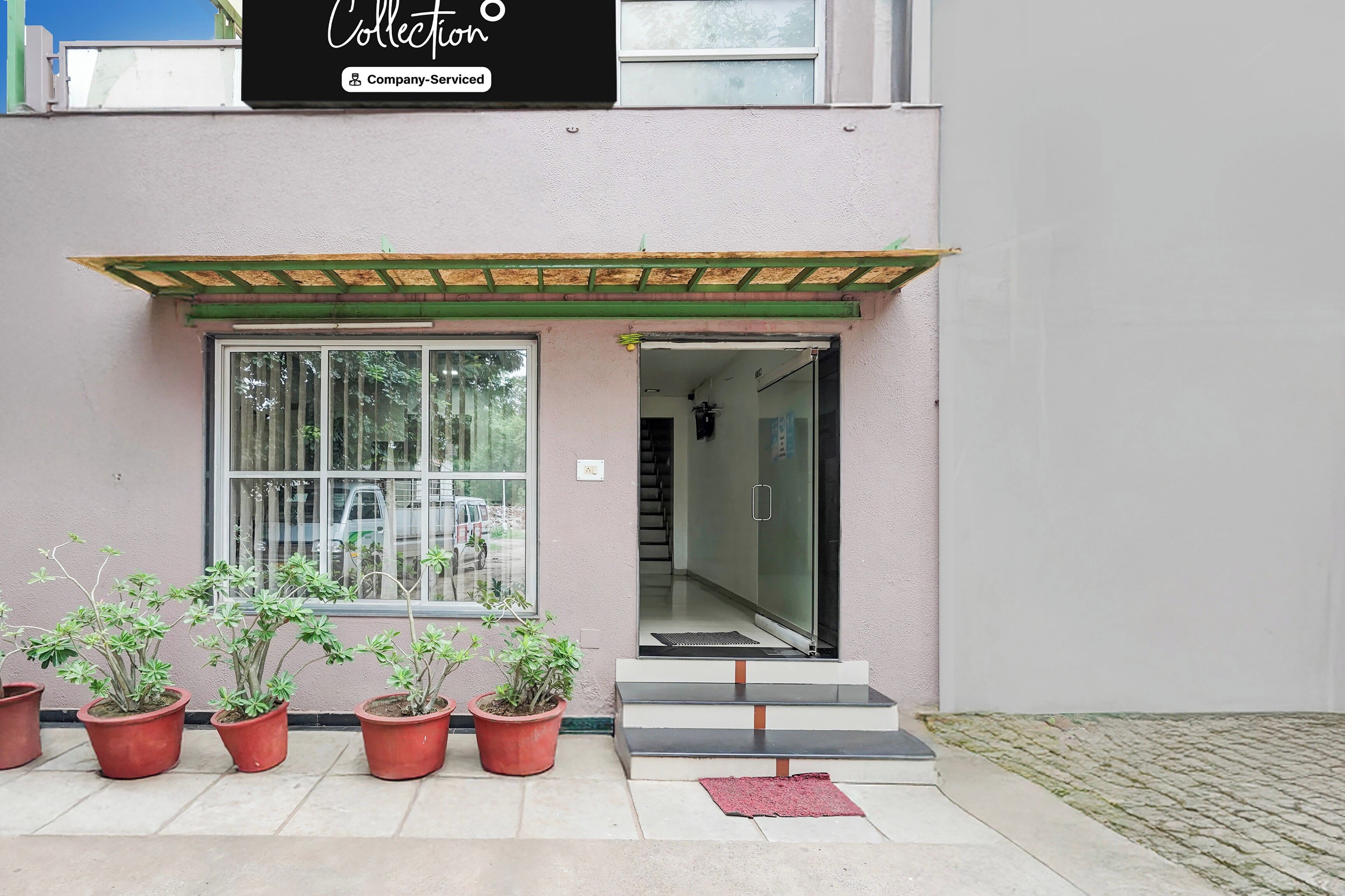 A building entrance with a glass door, potted plants, and a sign above.