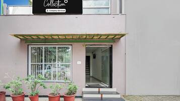 A building entrance with a glass door, potted plants, and a sign above.