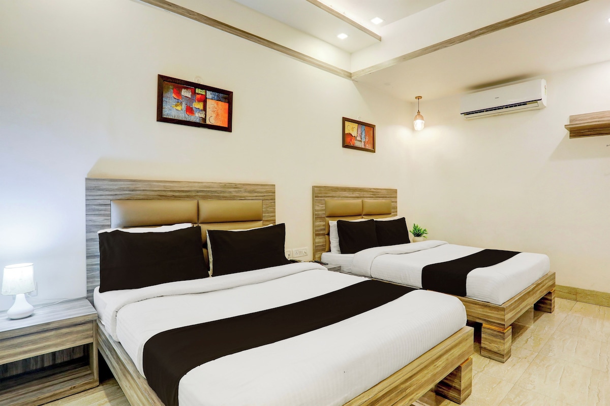 Habitación de hotel con dos camas, una mesita de noche, una lámpara y dos cuadros en la pared.