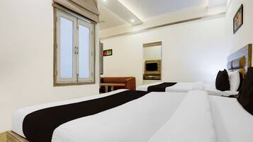 Een hotelkamer met twee bedden, een raam met gordijnen, een kleine tafel, een bank en een aan de muur bevestigde televisie.